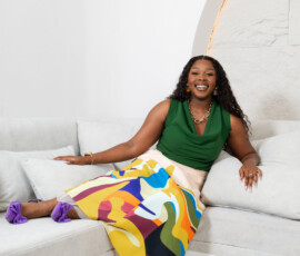 Expert styling highlighting bold color contrasts. Relaxed fashion shot of a model seated on a sofa wearing purple bow heels, a green top, and a K&R Thread patterned skirt.