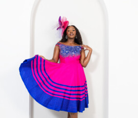 Vibrant fuchsia tones meet intricate artisan beadwork. A woman wearing a bright fuchsia pink midi dress with blue beaded neckline and matching fascinator from K&R Thread.