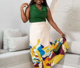 A statement of artistic elegance featuring the Abstract Maxi Set. Black woman modeling an emerald green sleeveless cowl neck top and a cream maxi skirt with bold yellow, blue, and maroon abstract print by K&R Thread.