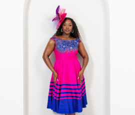 Artisan beadwork paired with a bold fuchsia silhouette. A woman standing in a vibrant hot pink sleeveless cocktail dress with blue floral beadwork and a matching headpiece by K&R Thread.