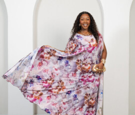 Designed for movement and sophisticated summer styling. A model showcasing the movement of a wide-sleeve floral kaftan in shades of orchid and plum from K&R Thread.