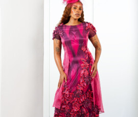 Artisan 3D floral appliqués create a stunning visual texture. A woman in a magenta and plum midi dress featuring 3D floral appliqués and a matching fascinator by K&R Thread.