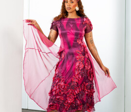 Intricate 3D floral detailing meets a flowing tea-length silhouette in shades of magenta. A woman posing in a magenta and purple tea-length dress with 3D floral appliques from K&R Thread.